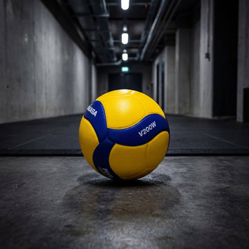 Odbojkarske žoge na tleh v gymu, rumena in modra, idealne za trening in tekme.